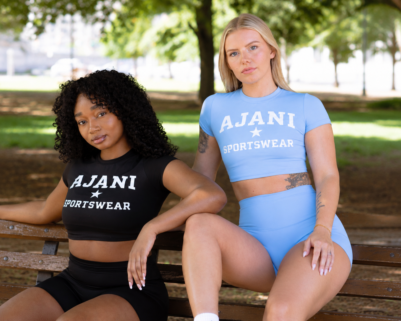 Two women wearing Ajani Sportswear crop tees and shorts on a park bench